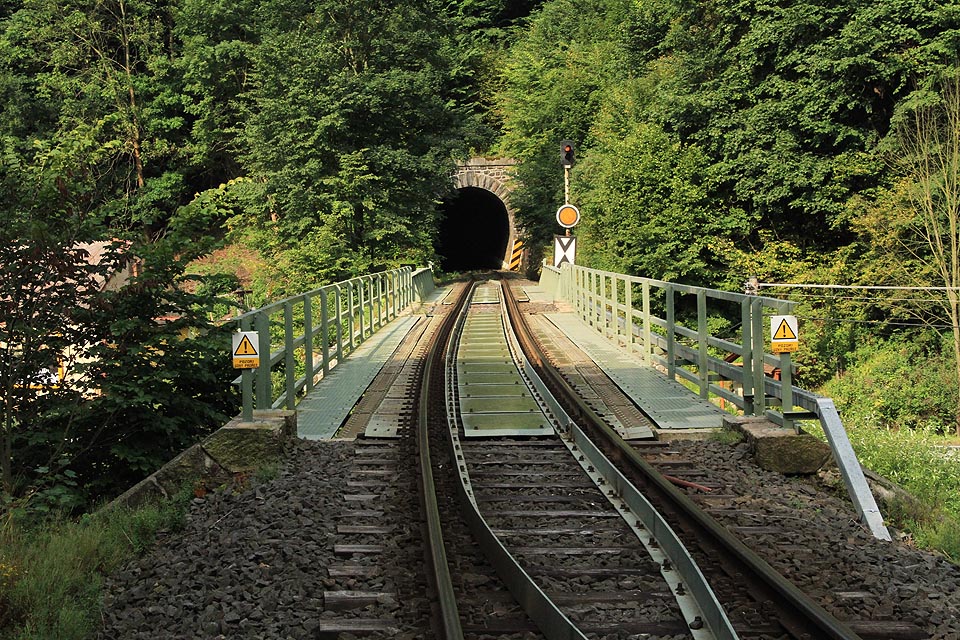 Příjezd k Bečovskému tunelu od severu, přes mosty nad řekou Teplou a silnicí č. 20 (E49). V srpnu 2015 probíhala výměna původních mechanických návěstidel ve stanici Bečov nad Teplou a na předvěsti byla instalována nepřenosná pevná návěst výstraha.