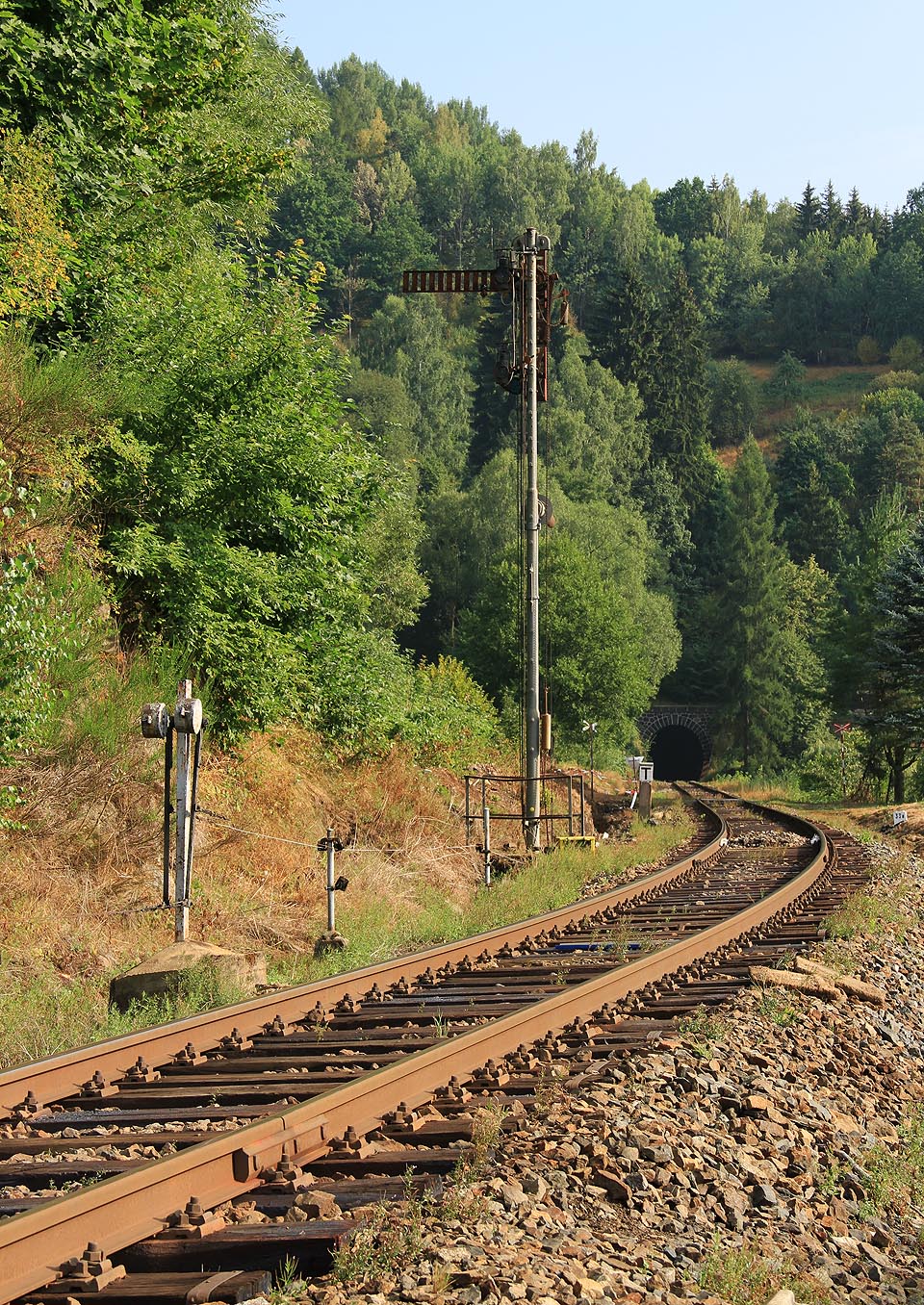 Pohled na romantické zátiší s mechanickým návěstidlem, tunelem, přejezdem a karbolem páchnoucími dřevěnými pražci z roku 2015 je dnes již minulostí.