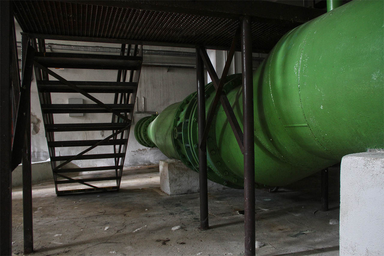 Roury jsou jako obrovští zelení červi propletení mezi betonovým sloupovím haly.