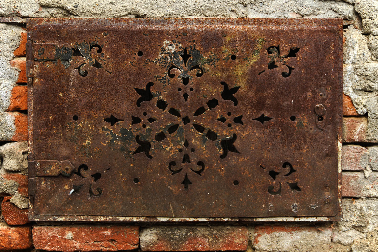 Skromný ornament na posledním zachovalém sklepním okénku je jedním z mála zdobných prvků na oprýskané fasádě domu.