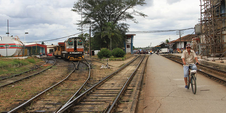 Pohled od západu. Doleva odbočují koleje nejstarší kubánské železnice vůbec - původní koňky do Nuevitas, rovně vedou koleje centrální dráhy mířící z Havany do Santiaga de Cuba na východě. V pozadí řídící věž a přejezd s ulicí Avellaneda, vlevo čerpací stanice.