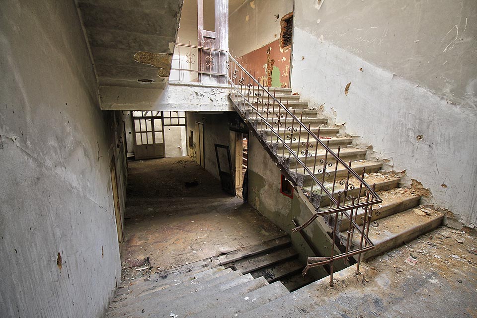 Velkoryse zasklené schodiště s kovaným zábradlím a kamennými stupni spojuje všechna patra budovy a dodává jí dojem velkoleposti.