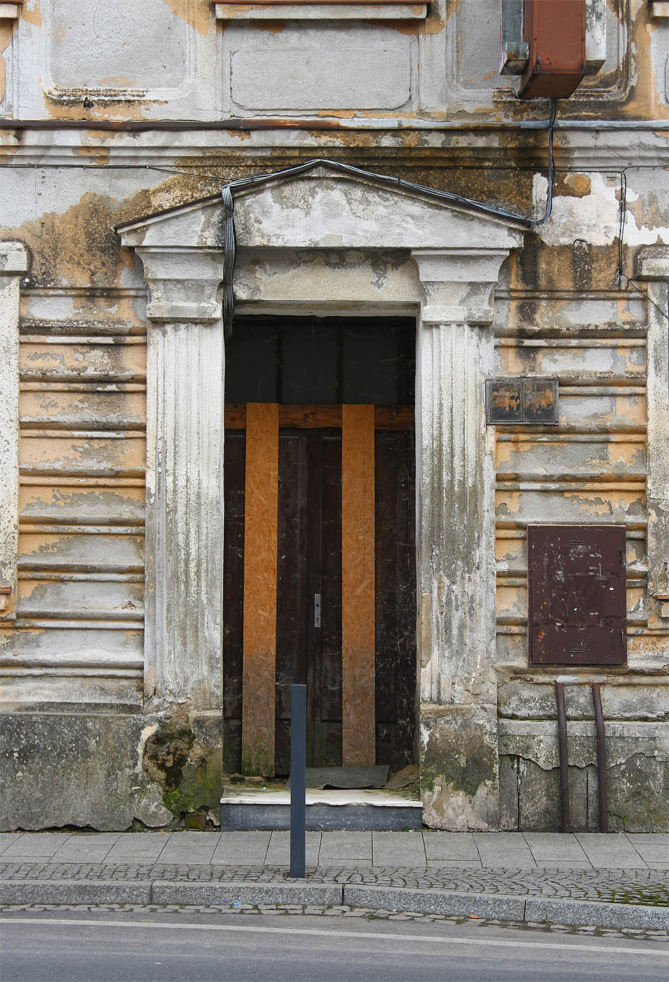 Pilastry ve stylu dórských sloupů rámují zatlučené a neprůchozí dveře. Přenesme se za ně alespoň ve své fantazii, která nám umožní průzkum hotelu.