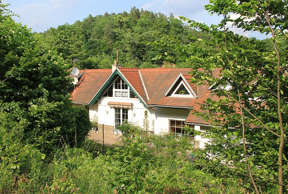 Pohled na budovu nádraží ze strany od kolejí zrušené dráhy. I po přestavbách lze rozeznat hlavní štít a kamennou podezdívku původní zastávky.