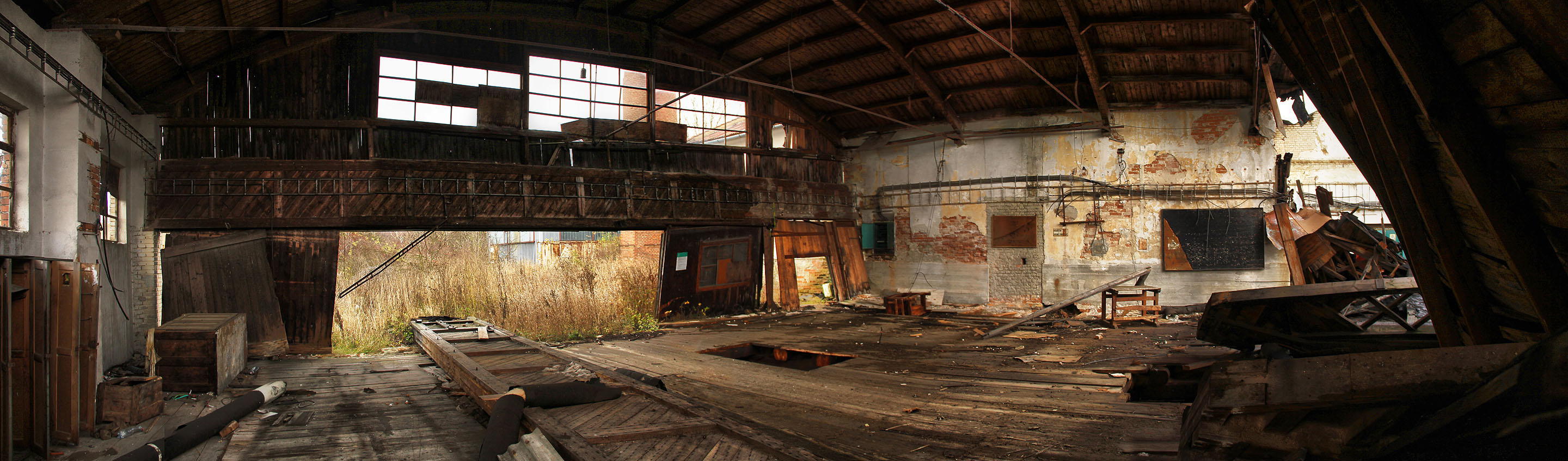Panoramatický snímek haly s částečně zřícenou střechou. Když se mezi budovami zvedne vítr, zdá se nám, jako bychom slyšeli ozvěnu katrů, které lačně porcují dřevo z okolních lesů.