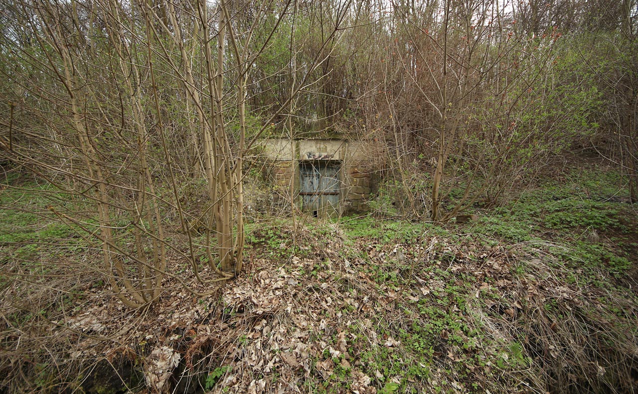 Přes odvodňovací strouhu za třetí staniční kolejí vede od kolejiště ke krytu betonová lávka zapadaná silnou vrstvou listí a zeminy.