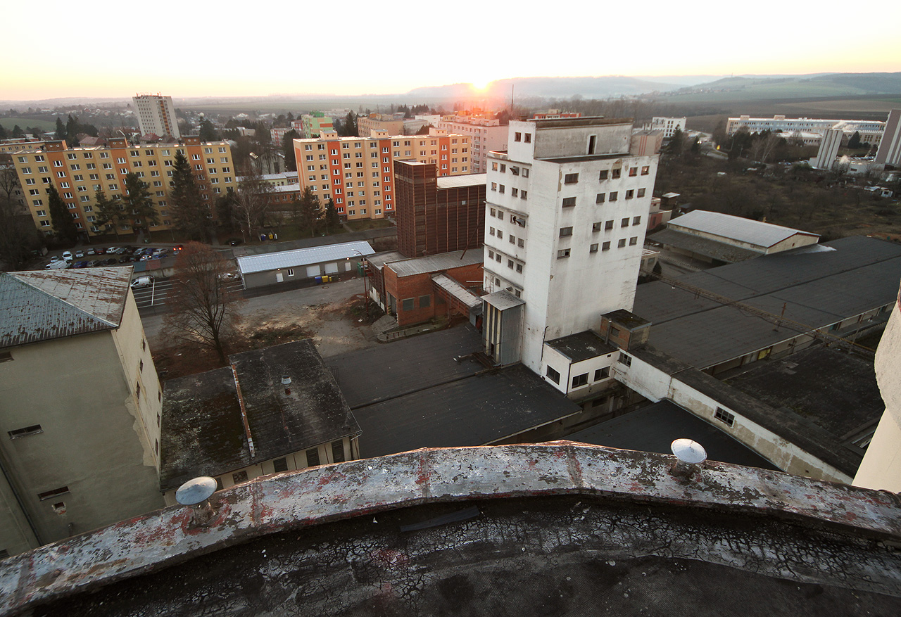 Pohled z nejvyšší budovy - sila - na bílou hrachárni a černou budovu s ocelovými nádržemi na krmné směsi vynikne nejlépe při západu slunce.