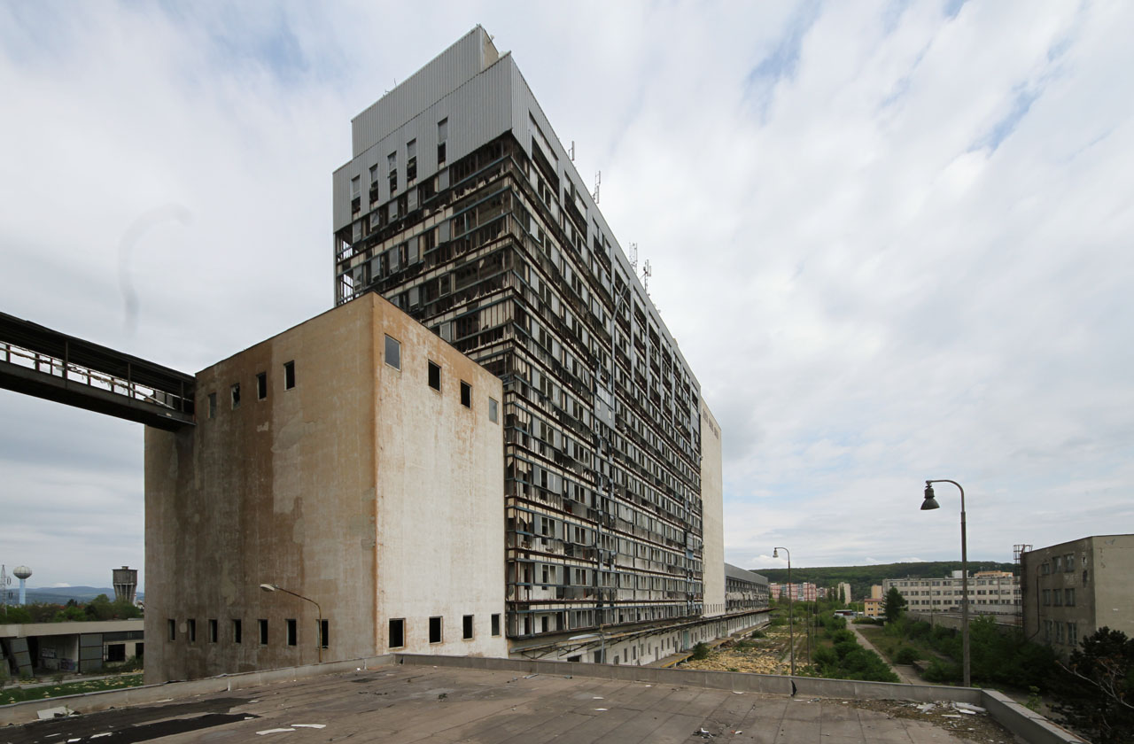 Pohled ze střechy nad krytou rampou pro vykládku obilovin a nakládku mouky nad trojicí kolejí železniční vlečky. Povšimněte si můstku spojujícího mlýn a silo na úrovni šestého patra.