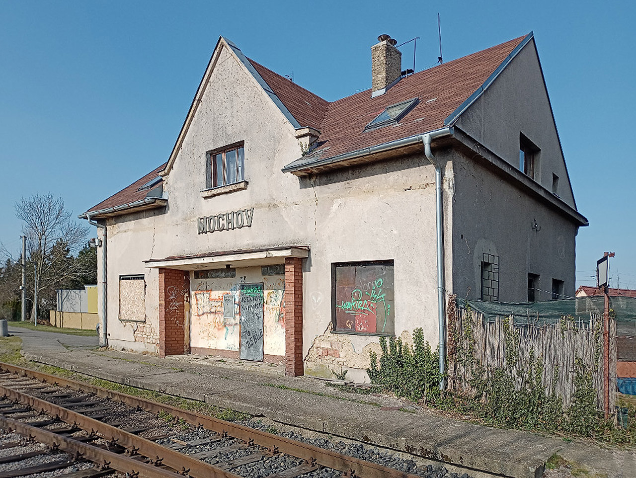 Staniční budova v Mochově je netypicky umístěna až na jihovýchodním zhlaví stanice. Před ní se nachází improvizované nástupiště z poněkud okoralých panelů.  Foto: Milan Koršo.