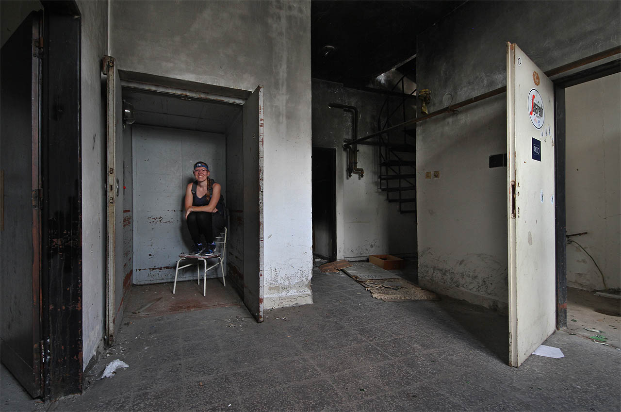 Pod schody se navždy zastavil nákladní výtah. Výtahářka se tak trošku nudí a sedíc na opěradle židle očekává své příští cestující.