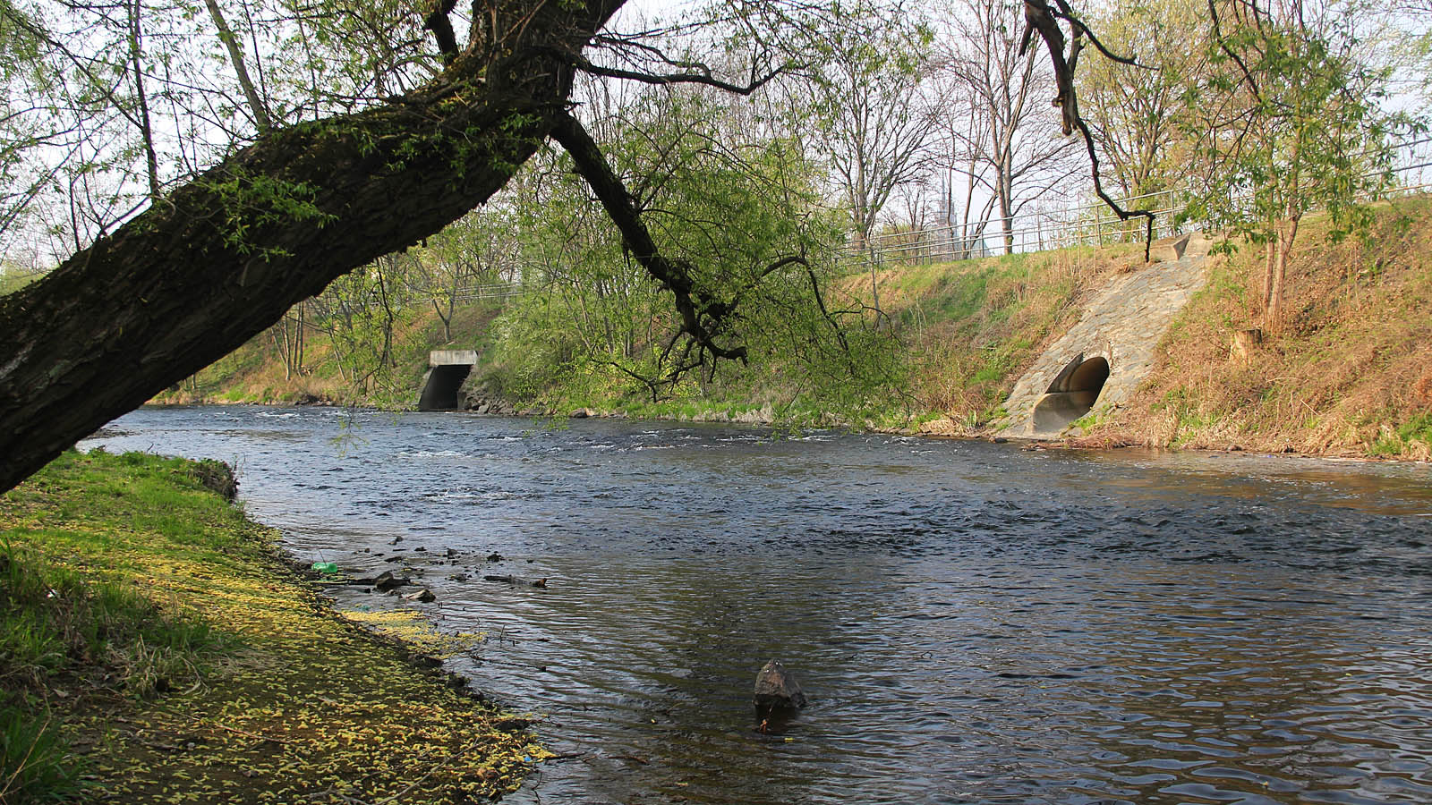 Pohled z pravého na levý břeh řeky Svratky pod hlavním nádražím v Brně. Vlevo je vidět ústí spojovací chodby z odlehčovací komory OKB04 k řece, vpravo pak ústí dešťové kanalizace z oblasti mezi ulicemi Trnitou a Opuštěnou - tedy z někdejšího ostrova mezi Svratkou a Svrateckým náhonem, na kterém stála mj. Offermannova továrna.