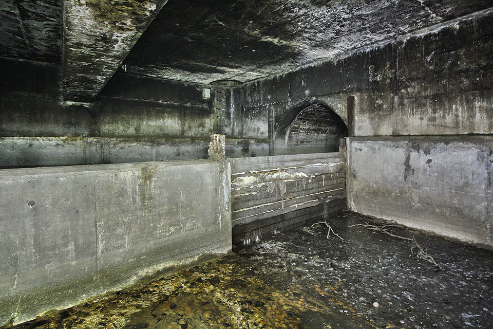 Dřevěnými dlužemi zahrazené koryto kmenové stoky B. Hrazení lehce prosakuje a špinavá voda se tak mísí s čistou říční vodou, která sem čas od času nateče při vyšším průtoku Svratky.