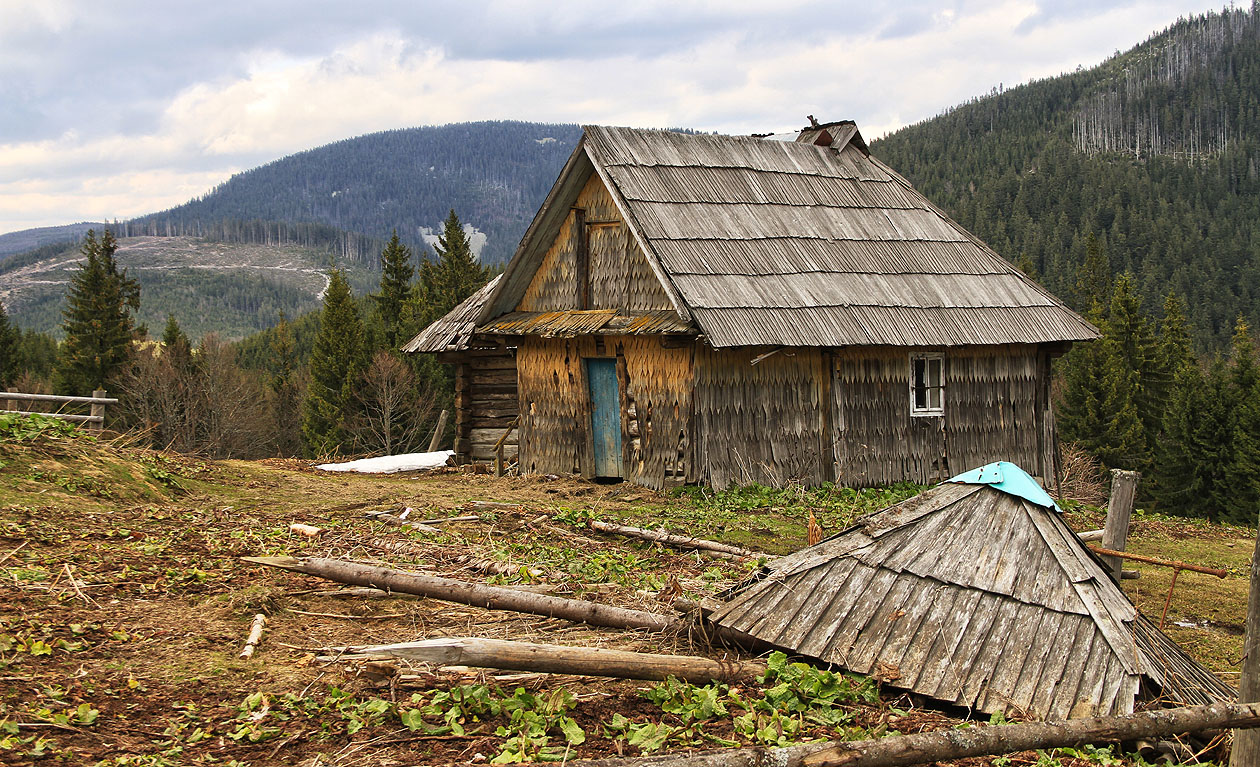 Zhroucený oboroh, ve kterém už dávno nikdo nesuší seno na pozadí nejmenšího a nejníže položeného z domků v osadě.