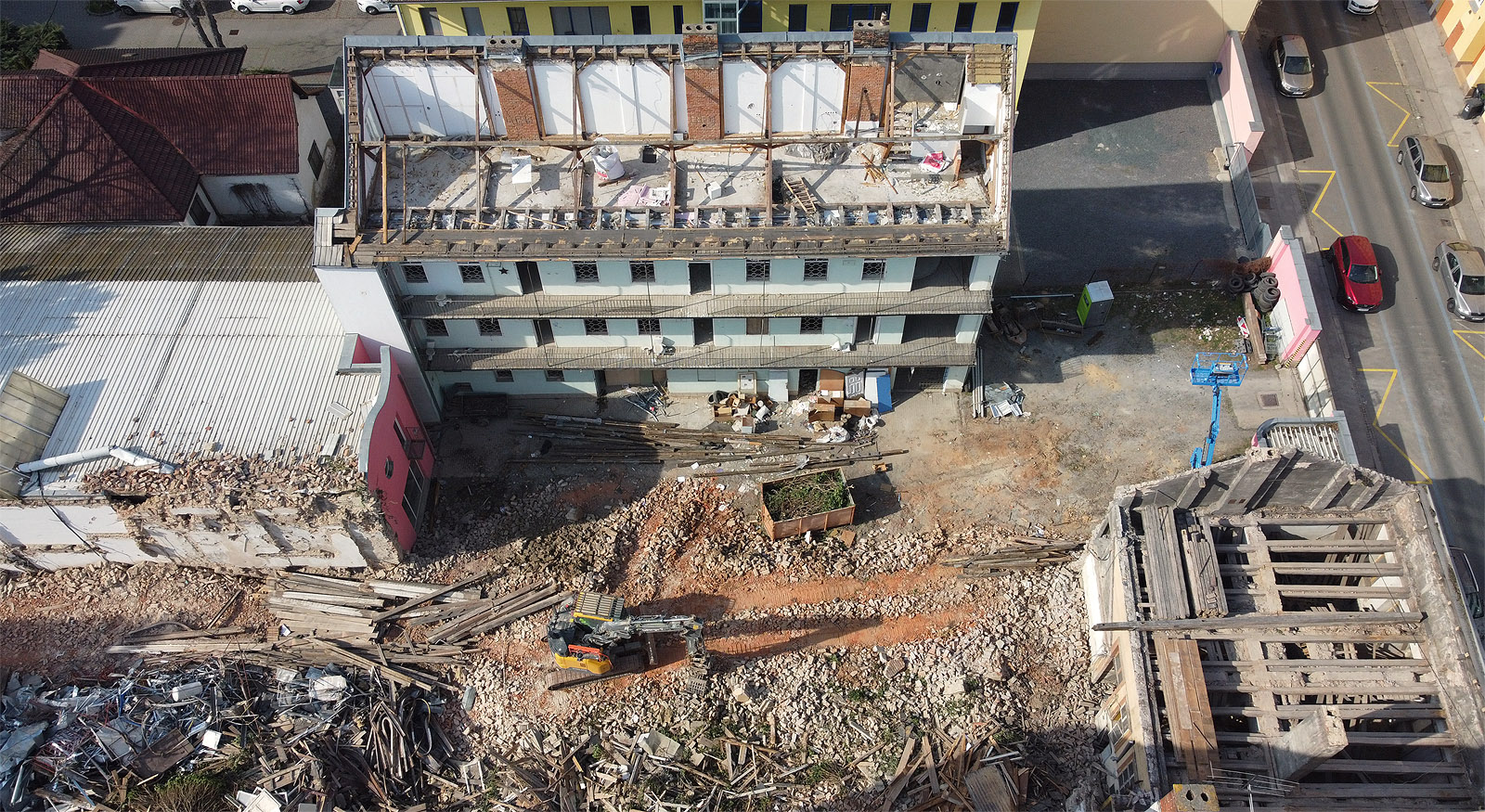 Letecký pohled od jihu. Dům Příční 14 je v pravém dolním rohu fotky, převážně hospodářské dvorní vestavby za ním už vzaly za své pod lžící bagru, který hoduje na jejich ruinách. Pavlačák Příční 12 zatím přišel jen o střechu, průčelní dům do ulice zmizel po zásahu americké bomby v roce 1944 a nikdy nebyl obnoven.