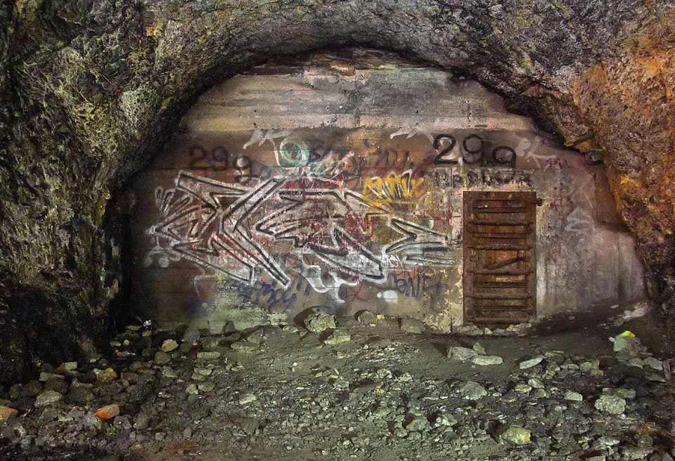 Další vstup do protiatomového krytu vede z dlouhé příčné štoly v západní části továrny. I když to tak nevypadá, je možné pokračovat plazivkou mezi stropem krytu a štoly.