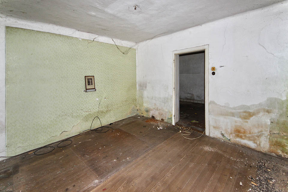 Obývací pokoj a ložnice současně odhaluje bídu zdejšího bydlení. Popraskané stěny a vlhká omítka nejsou ničím, po čem by kdokoliv toužil. Místo opravy však nyní dům čeká demolice.