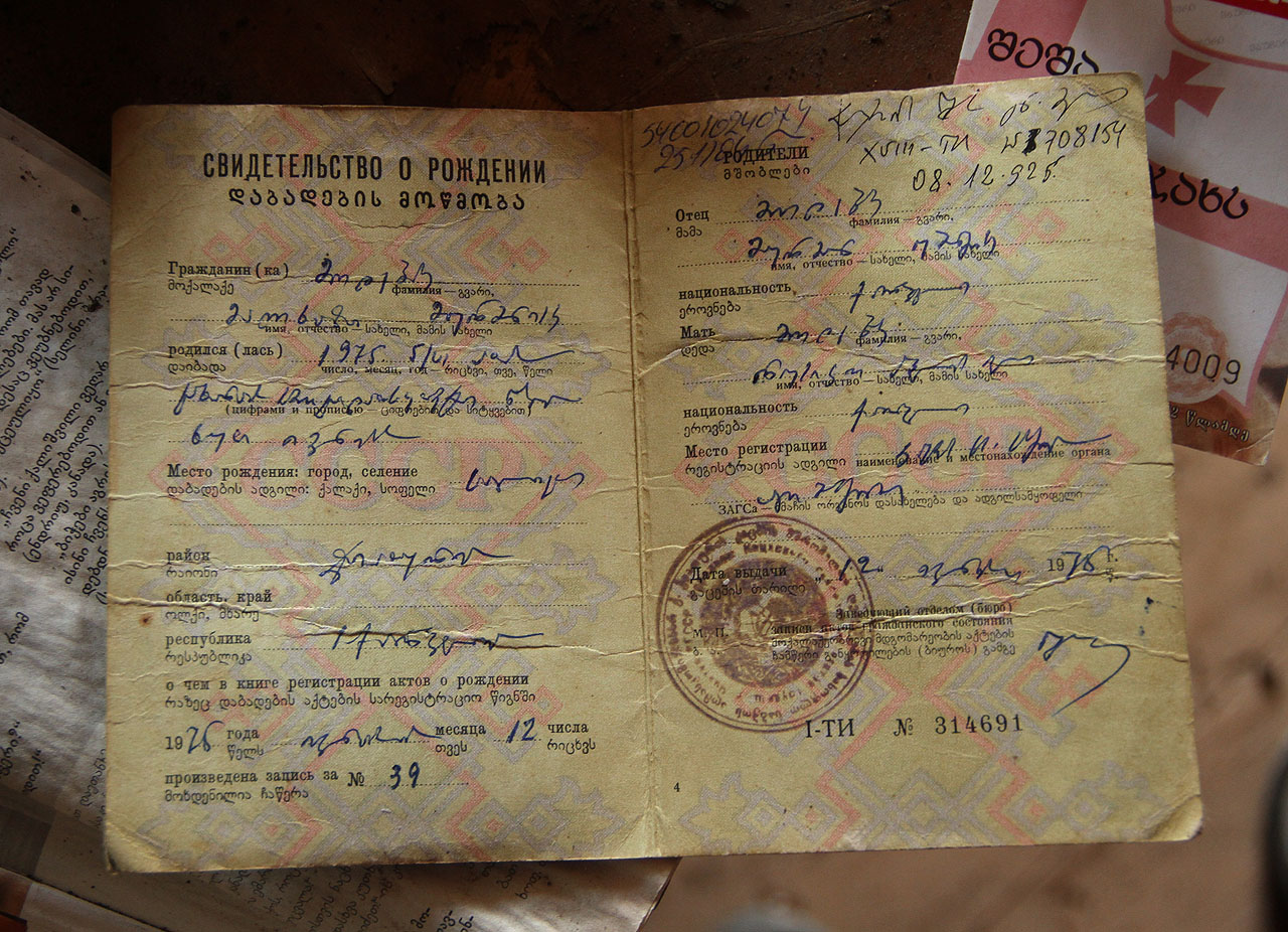 Jméno obyvatele domu narozeného v roce 1975 si může každý přečíst v zapomenutém rodném listě. Pokud ovšem zvládne přelouskat psací abecedu mchedruli. Rodných listů a maturitních osvědčení je tu několik a snad jen původní obyvatelé domu ví, proč si je před léty neodnesli s sebou.