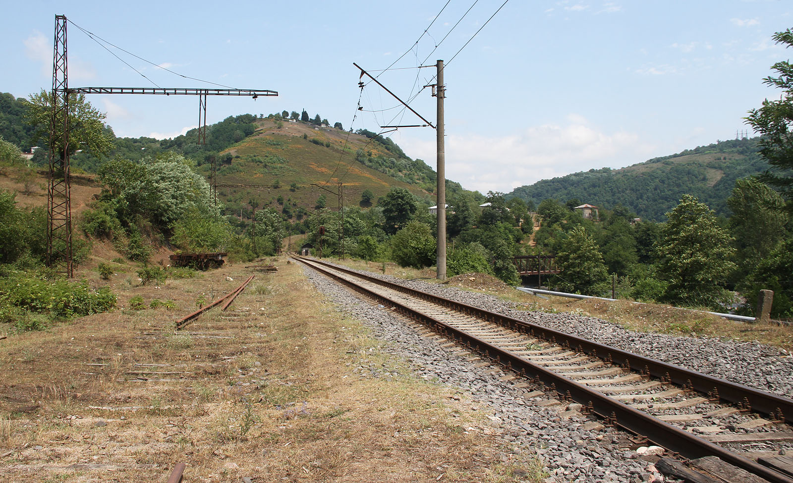Nad vytrhanou kolejí ještě zůstává konstrukce rezavého trakčního vedení. Drahé měděné dráty už byly demontovány.