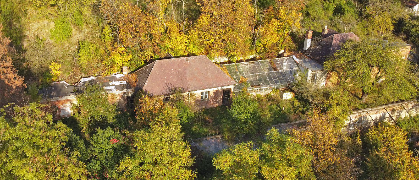 Letecký pohled na zanedbané a osiřelé skleníky, které i s hospodářskými přístavky a obytným domem vyhlíží svůj neslavný konec.