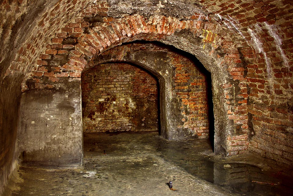 Skladovací prostory s vyztužovacíi pasy. Za posledním z nich se ukrývá průchod a okno vedoucí do kolmého sklepa pod obchůdkem.