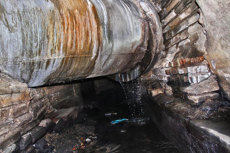 Průsak odpadních vod z kmenové stoky lemující levý břeh Svislače. Splašky tečou rovnou do řeky, kdo chce projít pod těžkou rourou, musí ohnout hřbet.