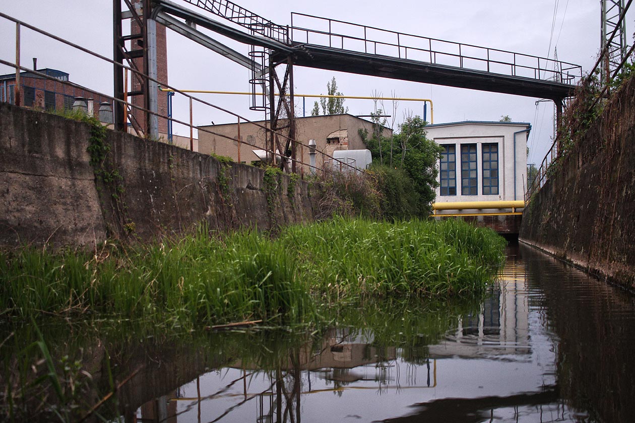 Konečně vyplouváme na povrch mezi areálem teplárny a náspem železniční trati. Budova, pod kterou jsme propluli, vypadá jako regluační stanice plynu. Nad hlavami se nám kříží potrubí, lávky a kabely.
