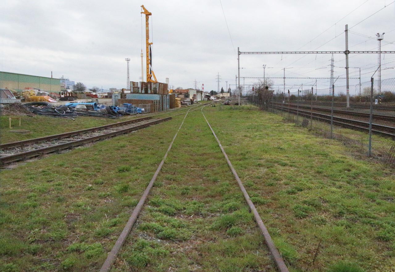 Protisměrný pohled k severu na současnou vlečku Firesty. V dálce jsou vidět baráky stojící od války na rampě překladiště mezi vlečkou a úzkokolejnou drahou.