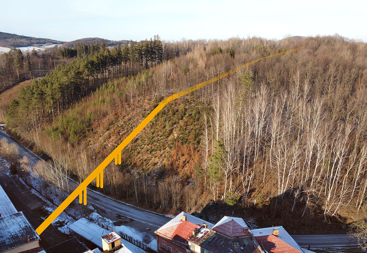 Odhad vedení drážky na základě nalezených betonových základů mostu přes silnici 1. třídy I/44, která za továrnou vypadá spíše jako místní komunikace. Dobře patrná je změna sklonu na horním konci paseky.
