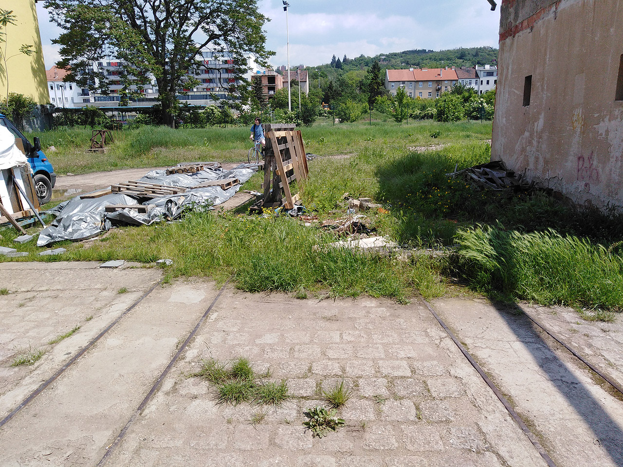 Za vydlážděným přejezdem se nachází trávník rostoucí na zbytcích suti ze zbourané haly.