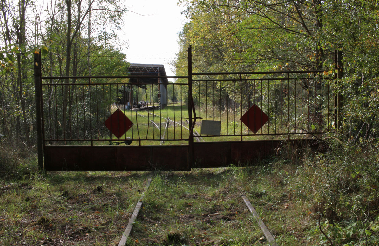 Pohled na vrata oddělující běžný prostor uvnitř bývalého vojenského objektu letiště od prostoru „za dvěma ploty“, ve kterém se nachází na předávkové a odevzdávkové koleji A2 krytý přístřešek pro stáčení kapalných paliv z železničních vozů. Paliva byla dále po prostoru letiště dopravována potrubím do opevněných palivových skladů.