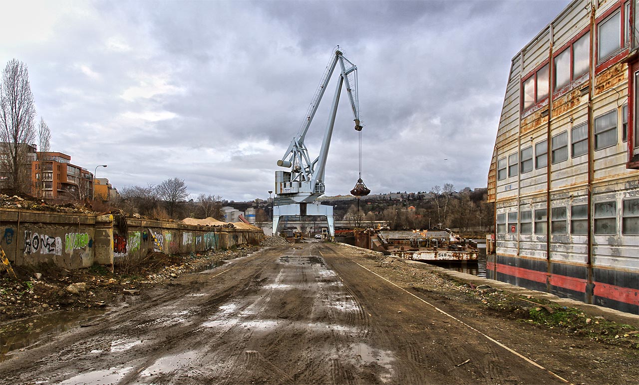 V dolní části přístavu lze pod smutným jeřábem stále nalézt v rozježděném bahně pásy kolejnic, které kdysi propojovaly Holešovice s celým světem. Ne na dlouho, výstavba luxusních bytů brzy dorazí i do míst, kde zatím kotví opuštěné staré lodě.