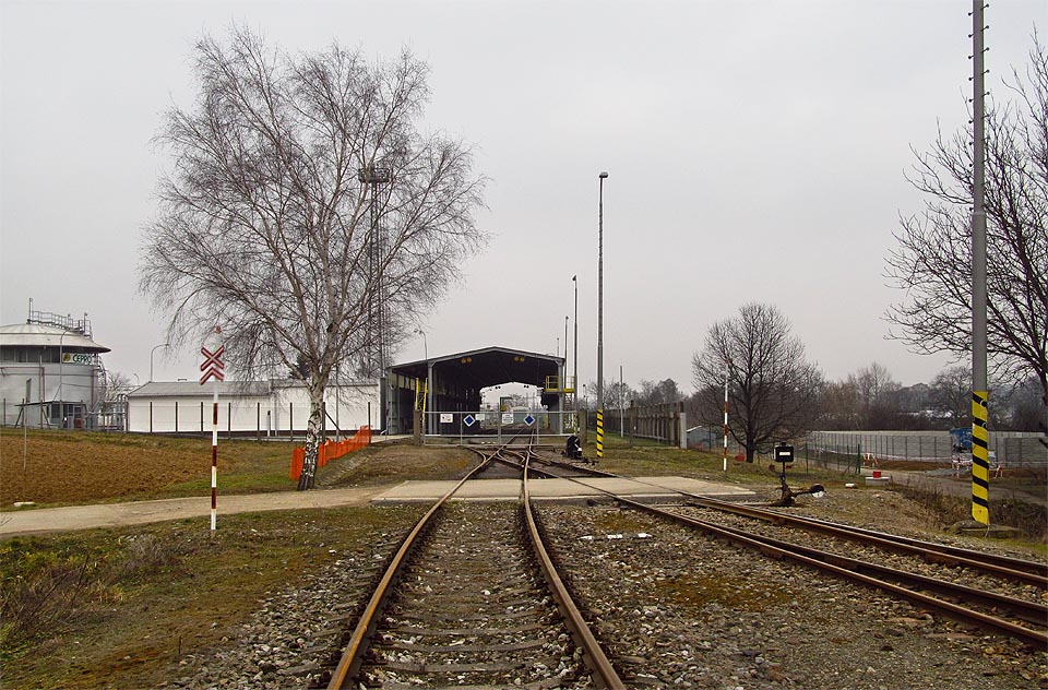 Před vjezdem do oploceného areálu kříží vlečku na nechráněném přejezdu místní komunikace.