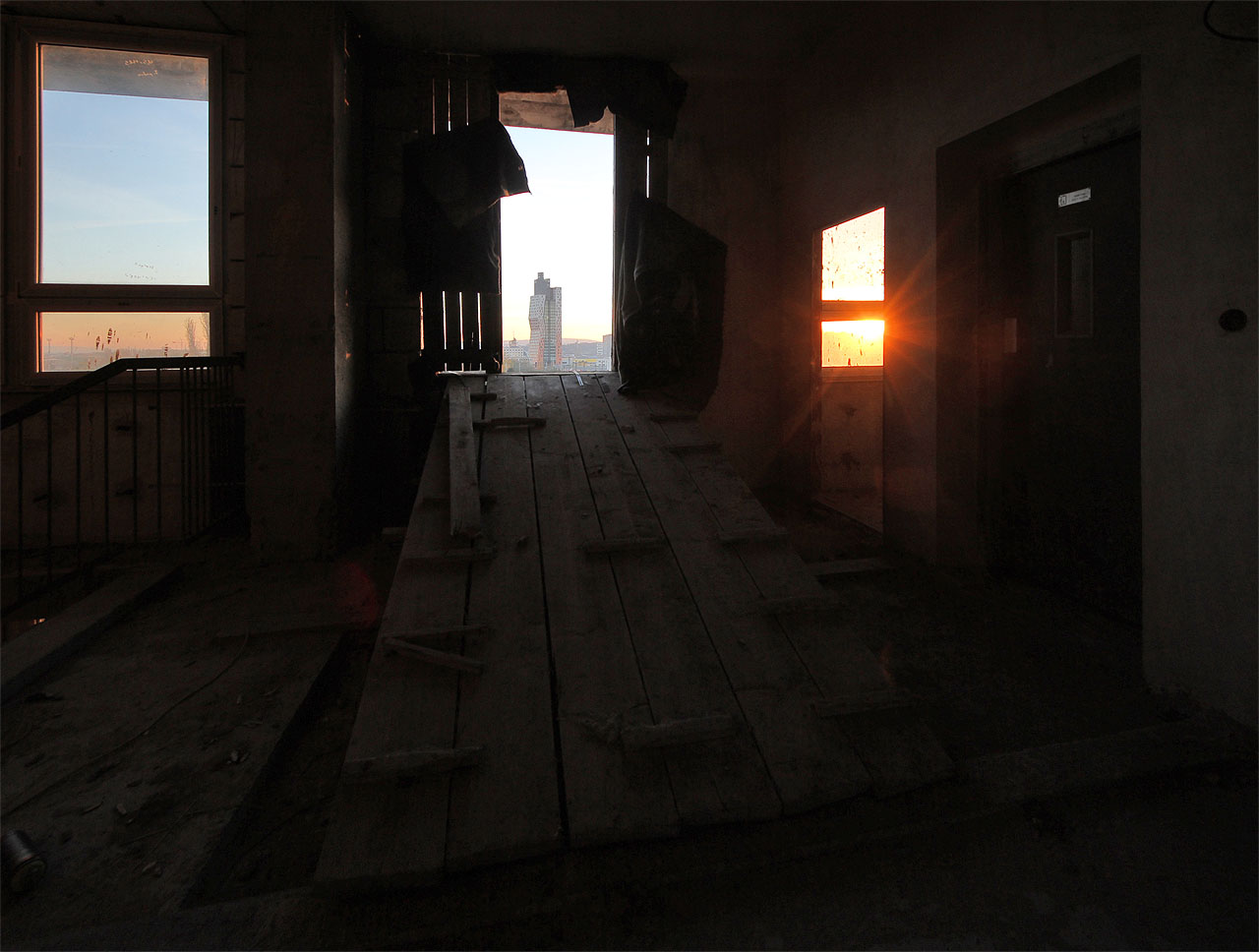 Pohled z nejvyššího patra přes takřka dějinnou propast. Nedokončená poliklinika měla být jednou z posledních velkých staveb období, které nenaplnilo své vize a skončilo neúspěchem a odmítnutím. Naproti tomu AZ tower je pýchou období následujícího, jež bez vizí mnohdy nedovede navázat na pozitivní odkazy z minulosti.