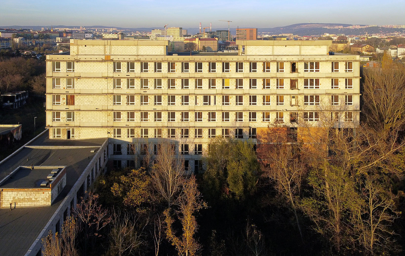 Čisté a téměř pravidelné tvary nedokončené nemocnice zjevně předběhly (alespoň v Brně) o třicet let čas. Přinejmenším tak usuzujeme při pohledu na osluněnou jižní fasádu, za kterou se v dálce vypíná stylově totožná fasáda kancelářské budovy Dorn. A nebo se tu jen za 30 let nic nezměnilo?