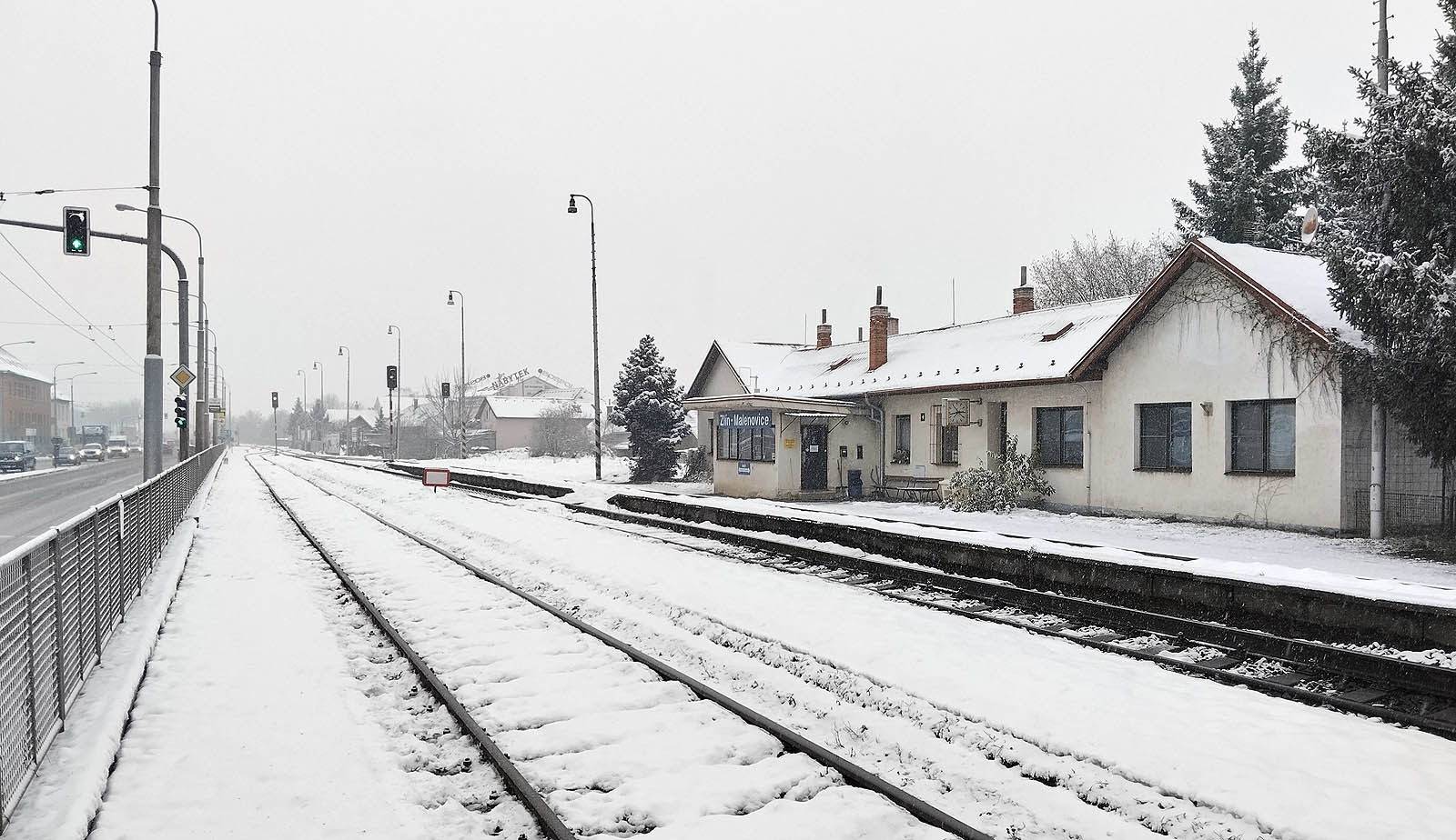 Celkový pohled na zasněženou stanici Zlín-Malenovice. Vlevo ubíhá třída 3. května, vpravo staniční budova s předsazenou dopravní kanceláří a bytem.